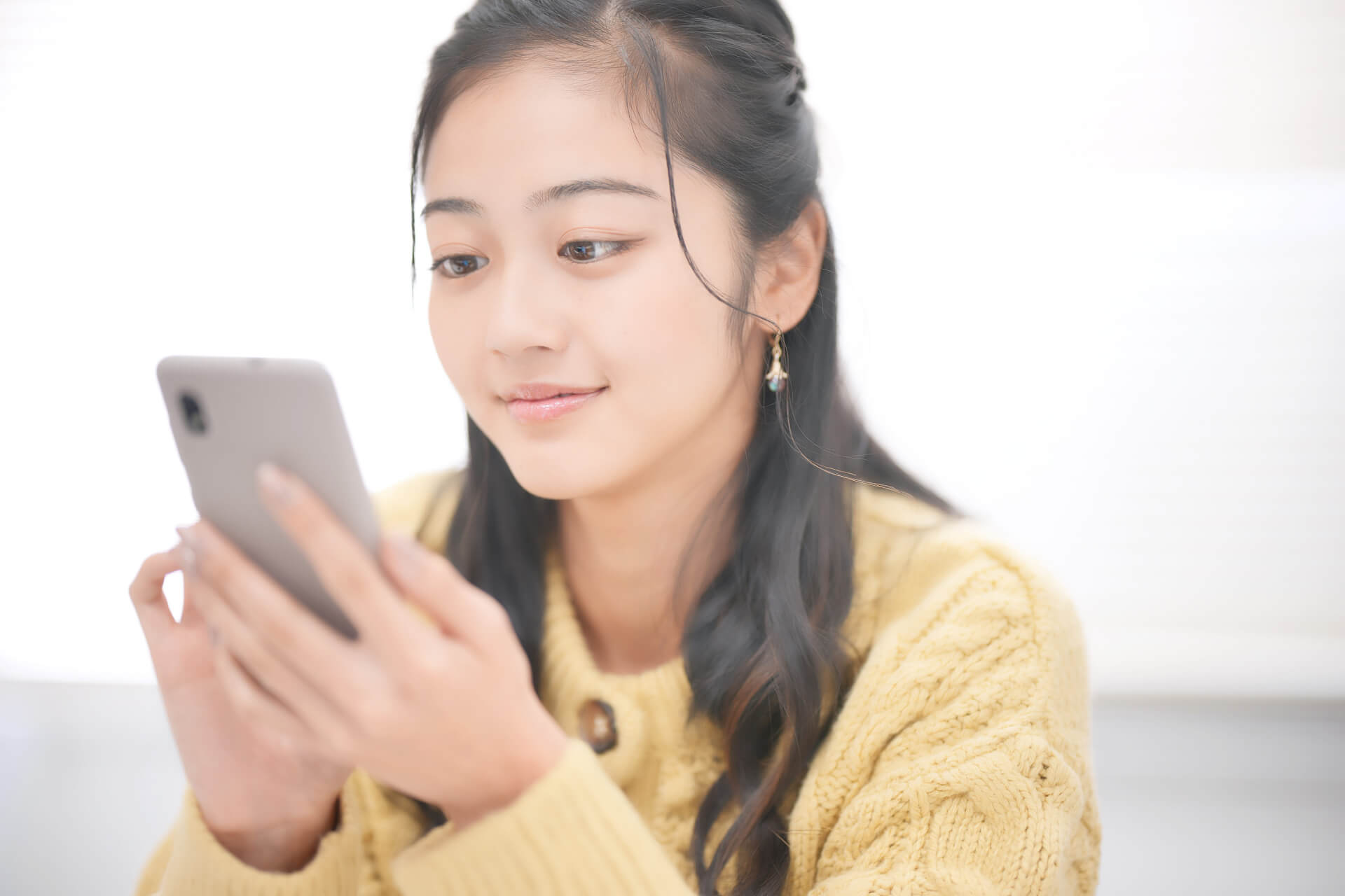黄色のセーターを着た女性がスマホを見る